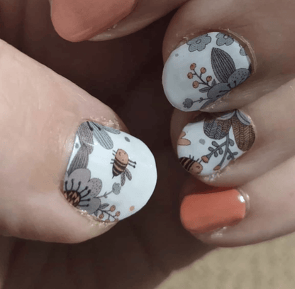 Close-up of bee and botanical nail wraps with peach accent nail on fingers