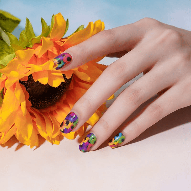 Hand with bright sunflower nail art wraps beside yellow sunflower showing floral nail design