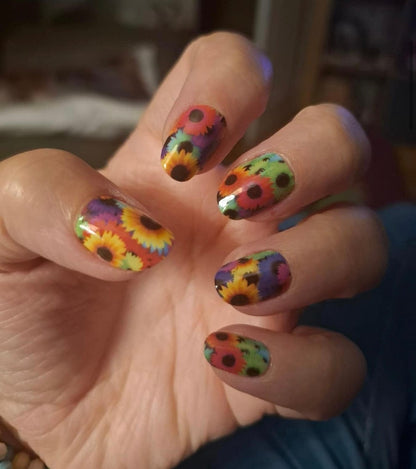 Vibrant multicoloured floral nail wraps on hand featuring sunflowers and bright rainbow patterns