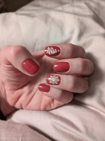 Red glossy Christmas nail wraps with white snowflakes worn on hand