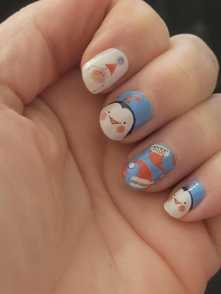 Cute cartoon penguin nail art wraps on hand featuring blue and white Christmas characters