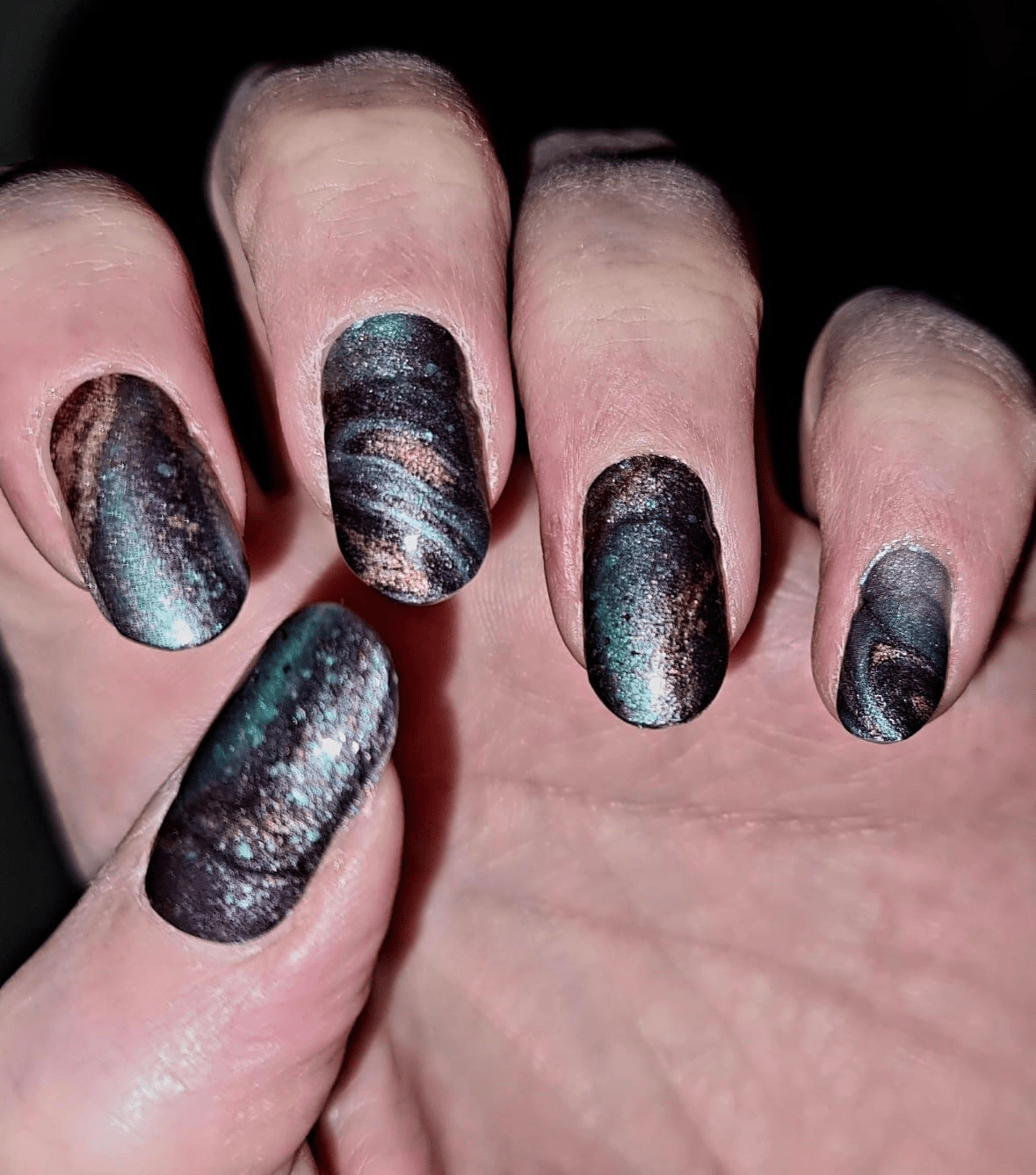 Ocean marble nail wraps in dark teal with gold shimmer on hand