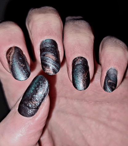 Ocean marble nail wraps in dark teal with gold shimmer on hand