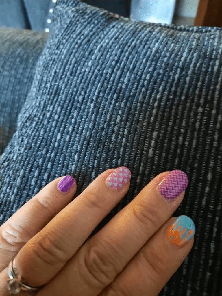 Close-up of geometric nail wraps on hand showing purple chevron turquoise orange drip nail art designs
