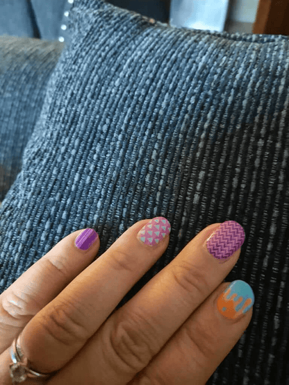 Close-up of geometric nail wraps on hand showing purple chevron turquoise orange drip nail art designs