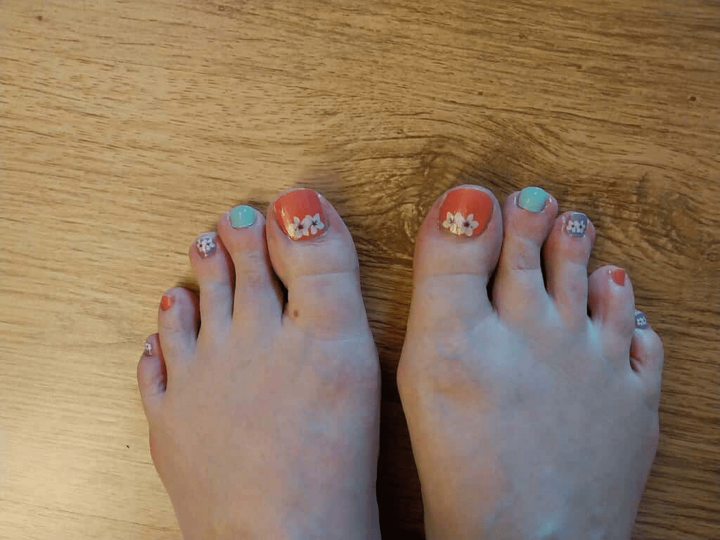 Pedicure nail wraps on feet showing coral orange green purple orchid floral design