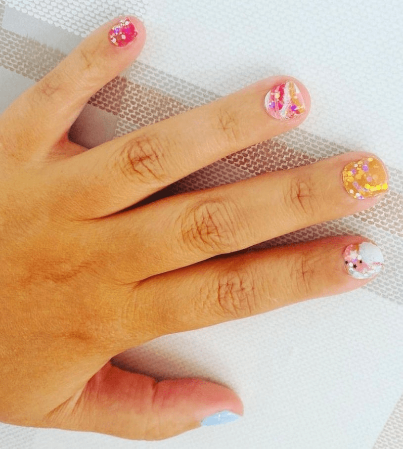 Hand displaying colourful paint splatter nail wraps with metallic gold accents and artistic brushstroke patterns
