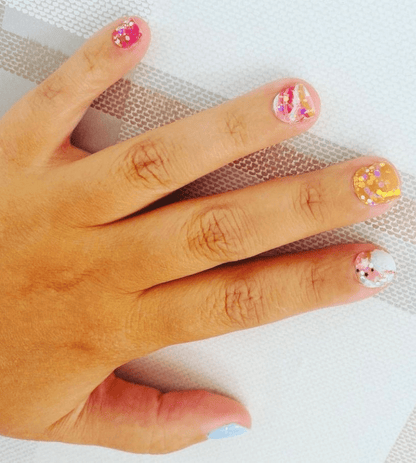 Hand displaying colourful paint splatter nail wraps with metallic gold accents and artistic brushstroke patterns