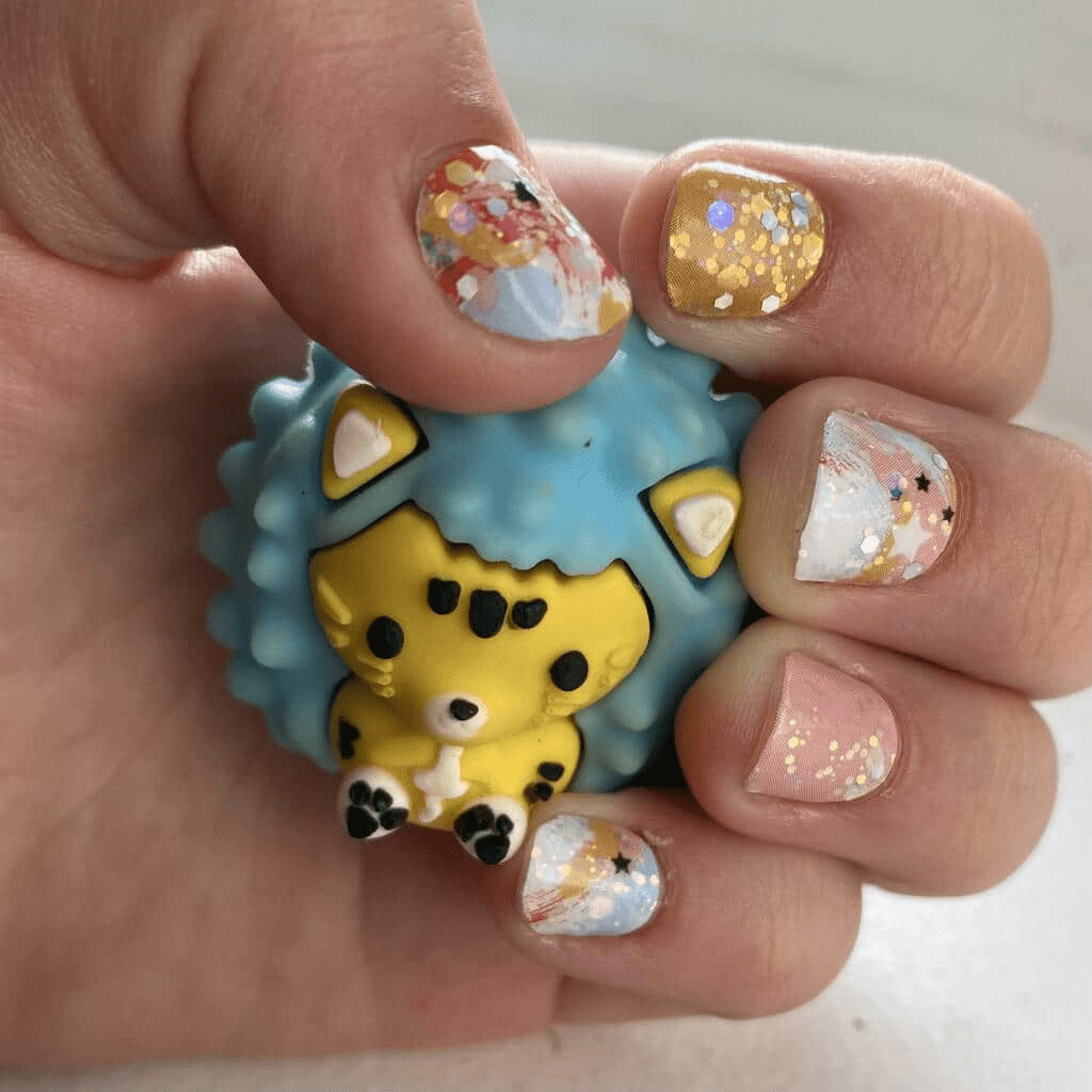 Hand holding cute hedgehog toy showing watercolour nail wraps with gold glitter and pastel paint effects