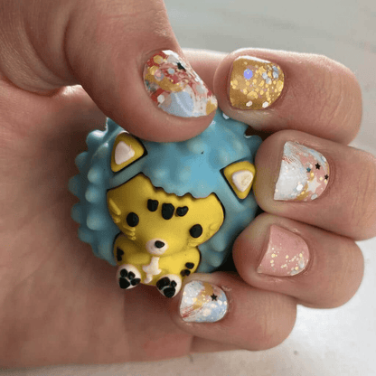 Hand holding cute hedgehog toy showing watercolour nail wraps with gold glitter and pastel paint effects