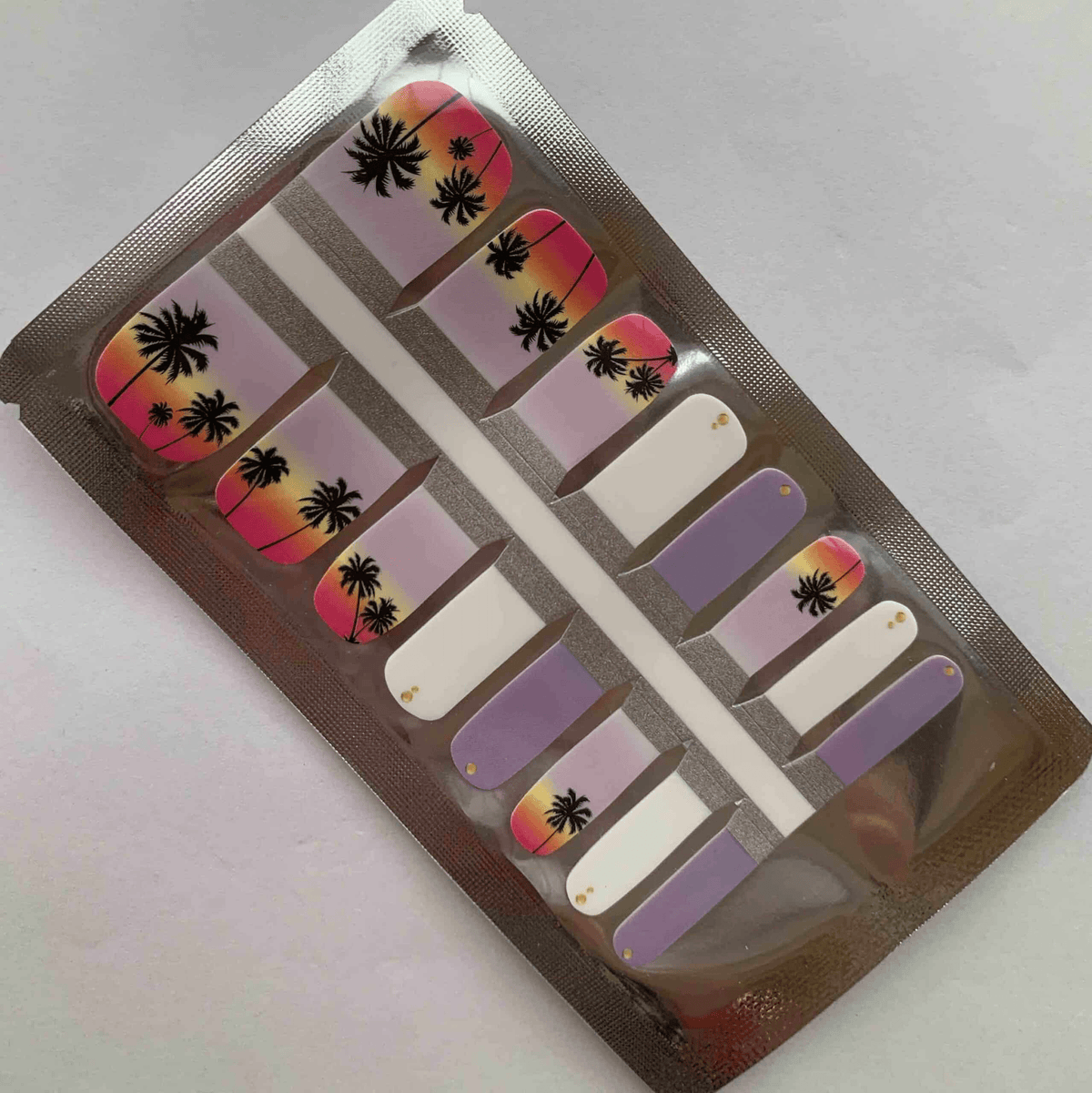 Purple and coral sunset gradient pedicure nail wraps with black palm tree silhouettes in package