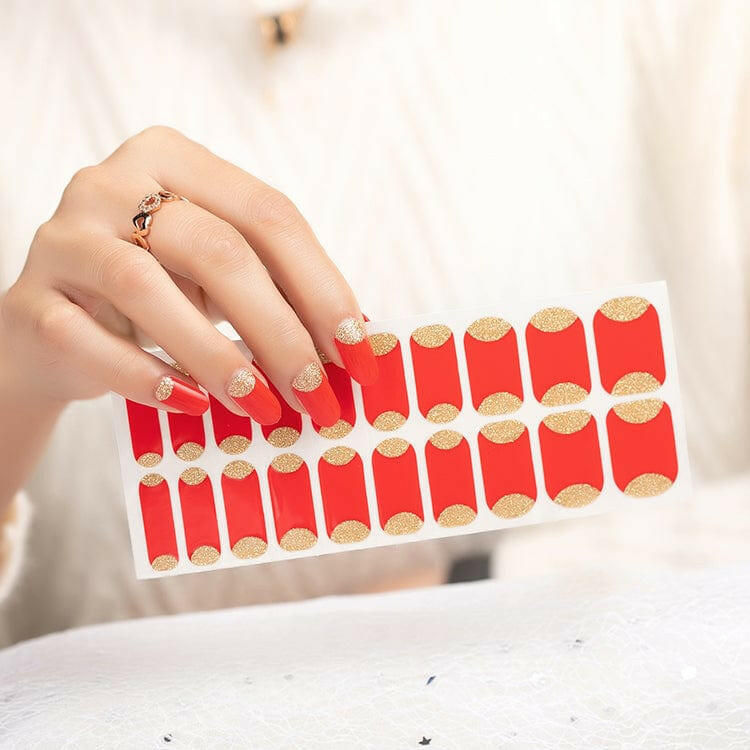 Hand holding red nail wraps with gold glitter reverse French tips for festive manicure