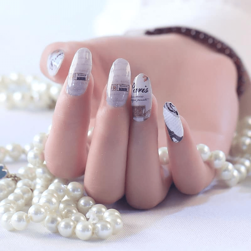 Hand wearing vintage Paris nail wraps featuring Eiffel Tower and rose patterns with pearls