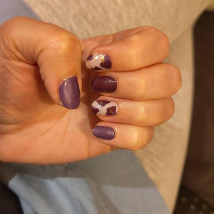 Deep purple nail wraps with nude accent nails featuring cow print and gold flecks