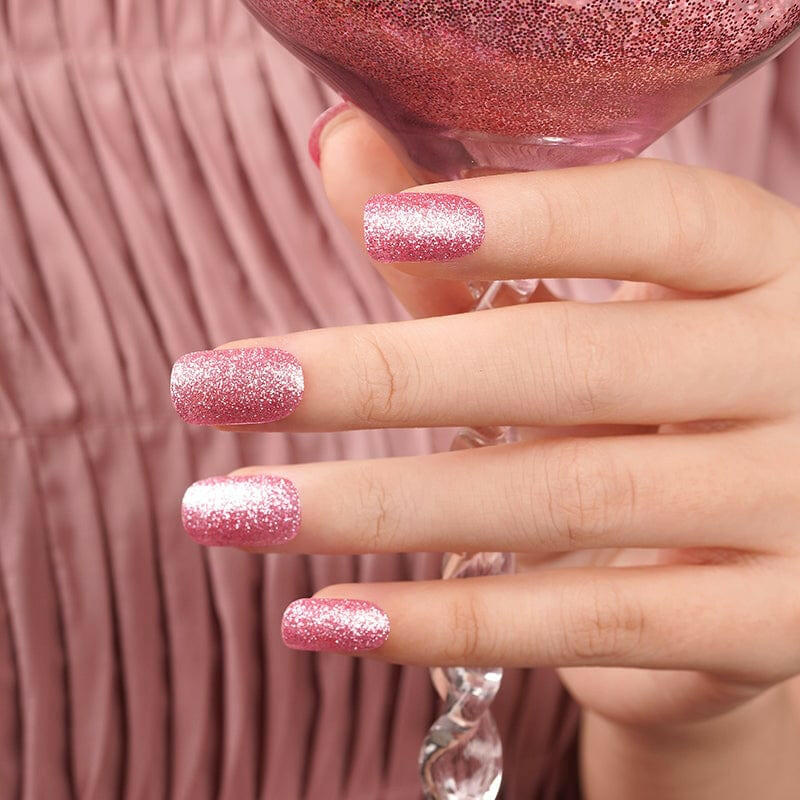 Hand with pink glitter nail wraps in a square shape, holding a glass