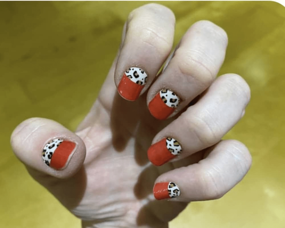 Hand wearing red nail wraps with black and white leopard print tips