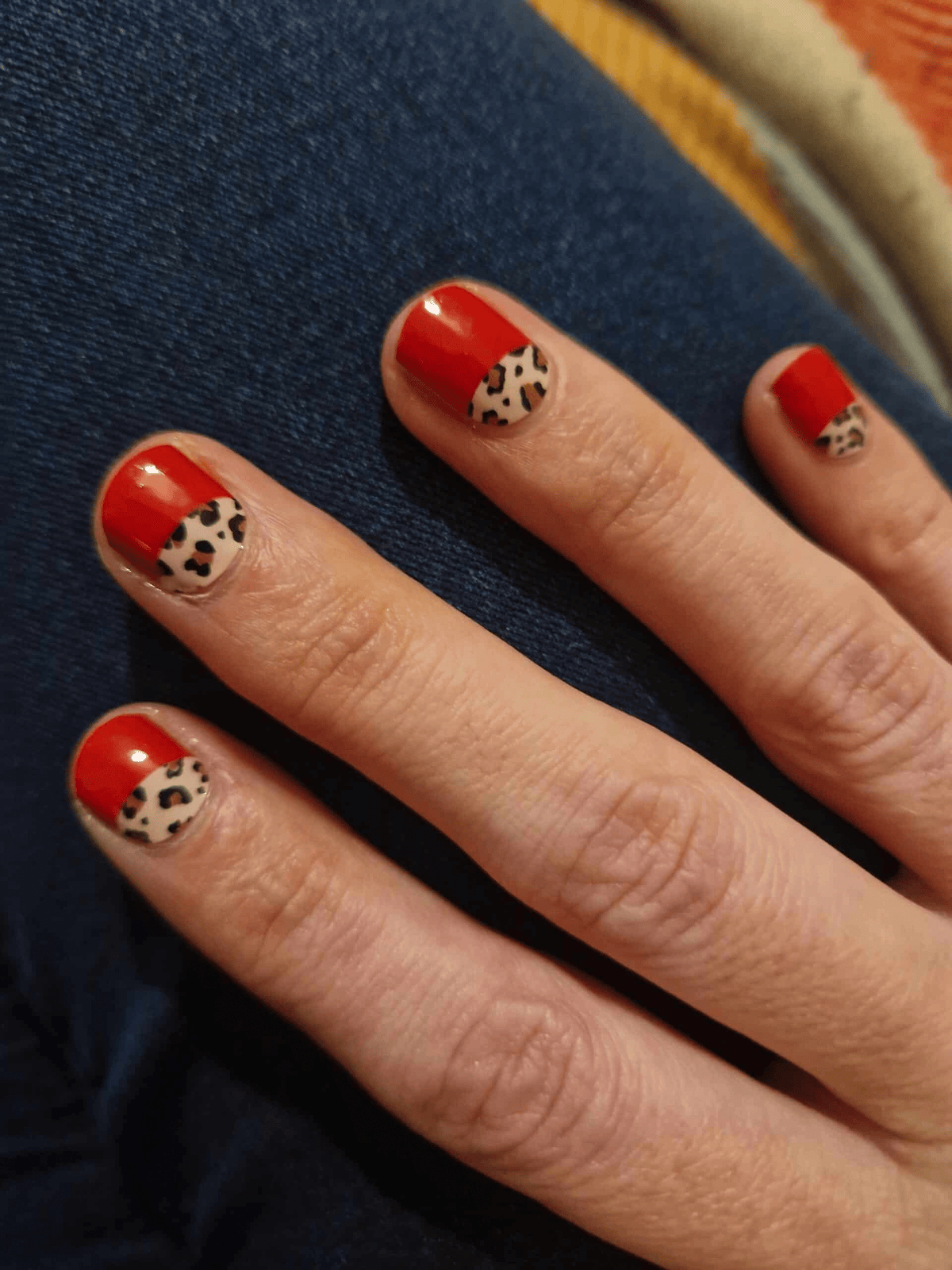 Four fingers showing red glossy nail wraps with animal print accent tips