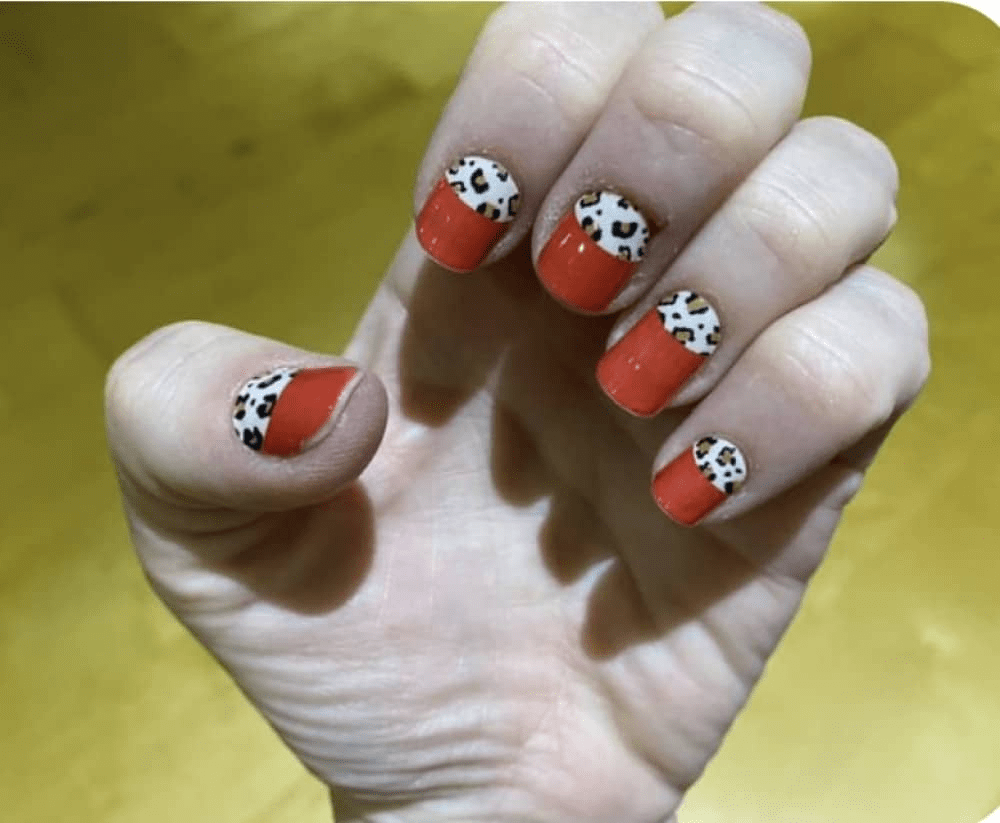 Hand displaying red nail wraps with leopard print French tip manicure design