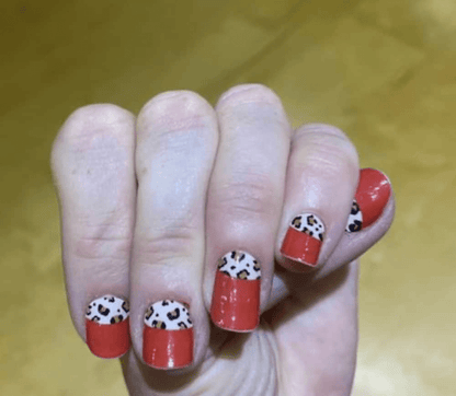Fingertips showing red glossy nail wraps with black white leopard print accents