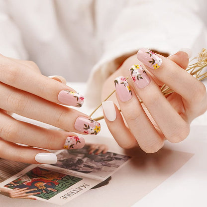 Hands displaying floral nail wraps with delicate pink flower patterns for spring manicure
