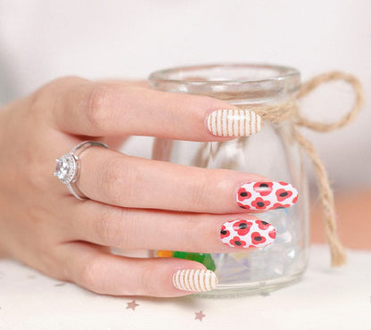 Hand wearing red poppy nail art wraps with striped accent nails holding glass jar