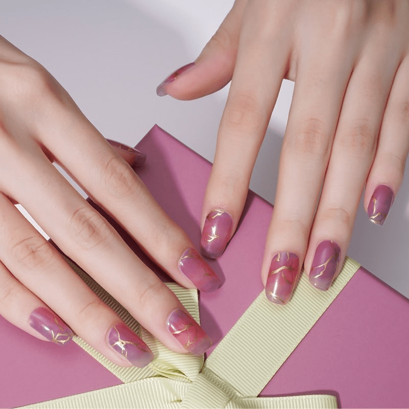 Pink marble nail wraps with gold veining on hand displaying elegant manicure design
