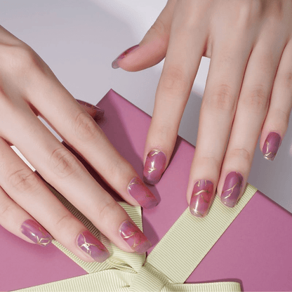 Pink marble nail wraps with gold veining on hand displaying elegant manicure design