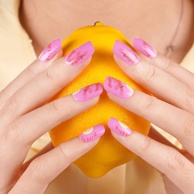 Hands holding orange showing pink prawn nail wraps for summer manicure