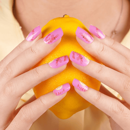 Hands holding orange showing pink prawn nail wraps for summer manicure