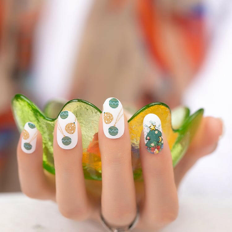 Hand wearing festive nail wraps with Christmas tree patterns and green bauble designs for holiday manicure