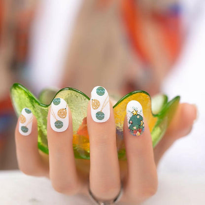 Hand wearing festive nail wraps with Christmas tree patterns and green bauble designs for holiday manicure