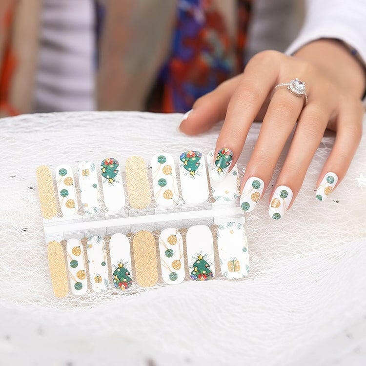 White Christmas nail wraps with green tree and gold bauble designs displayed on marble surface