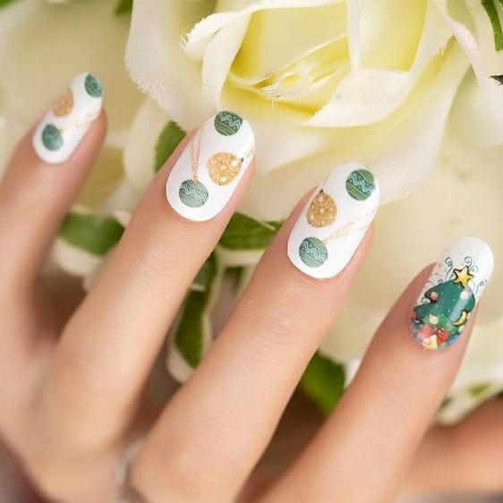 Christmas nail art on hand with white nail wraps featuring green baubles and festive tree designs