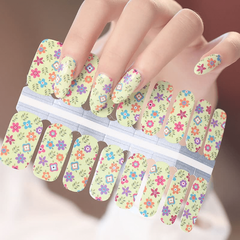 Colourful floral nail wraps on hand featuring tiny spring flowers on cream background