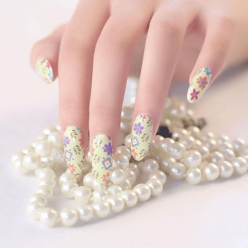Hand wearing pastel floral nail wraps with botanical garden pattern on white background