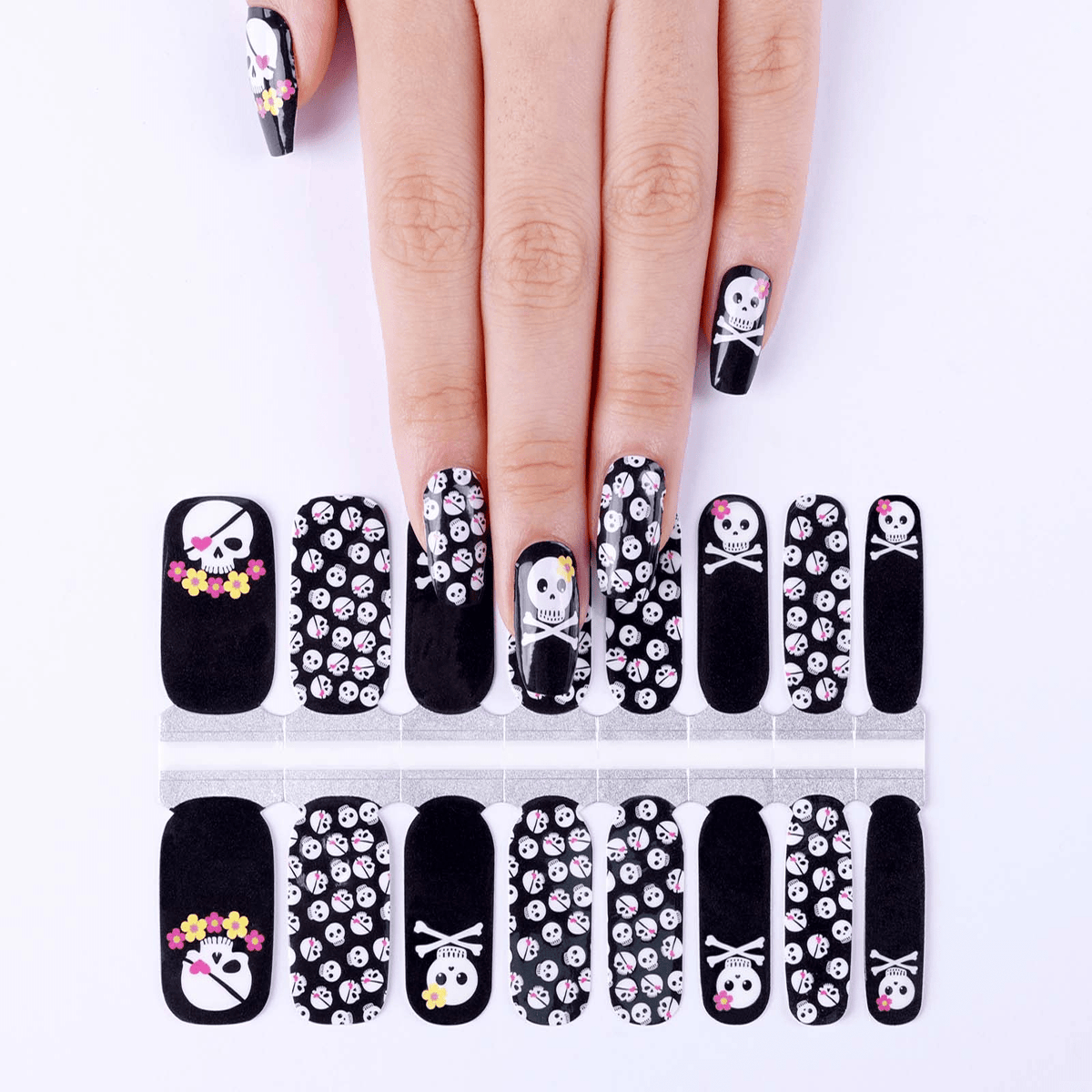 Hand wearing black skull nail wraps with pink crossbones gothic nail art design