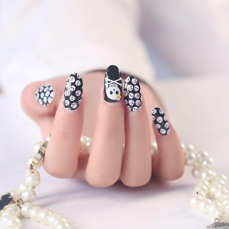 Black nail wraps with white skull and crossbones pattern on hand with pearl bracelet