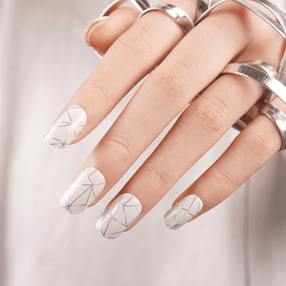 Hand with silver rings wearing geometric chrome nail wraps with reflective angular design