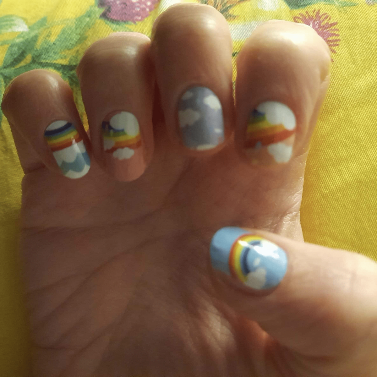 Nail wraps with rainbow and fluffy cloud designs on white and blue sky backgrounds