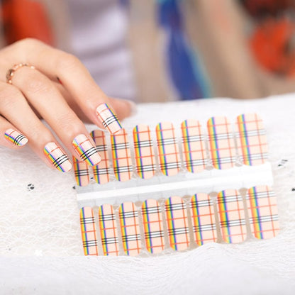 Hand holding rainbow plaid nail wraps with multicoloured stripes and geometric pattern design