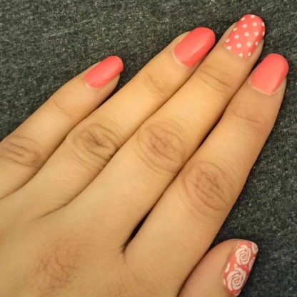 Coral pink nail wraps on hand with white polka dots and rose pattern nail art