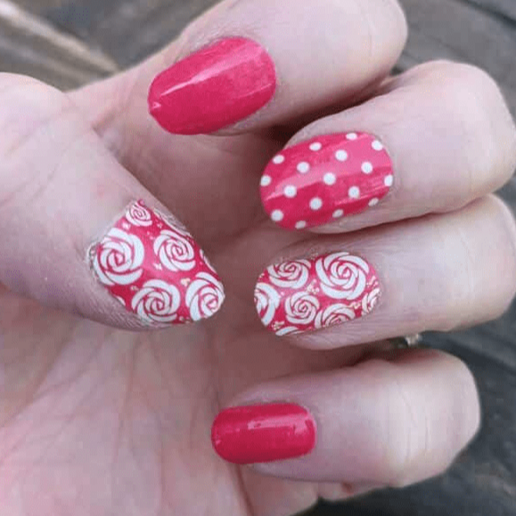 Hand wearing red and white nail wraps featuring rose patterns and polka dot designs