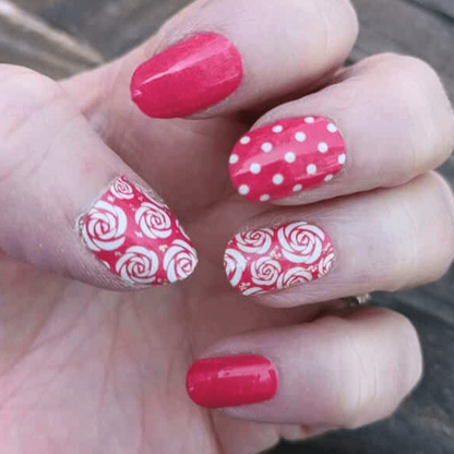 Hand wearing red and white nail wraps featuring rose patterns and polka dot designs