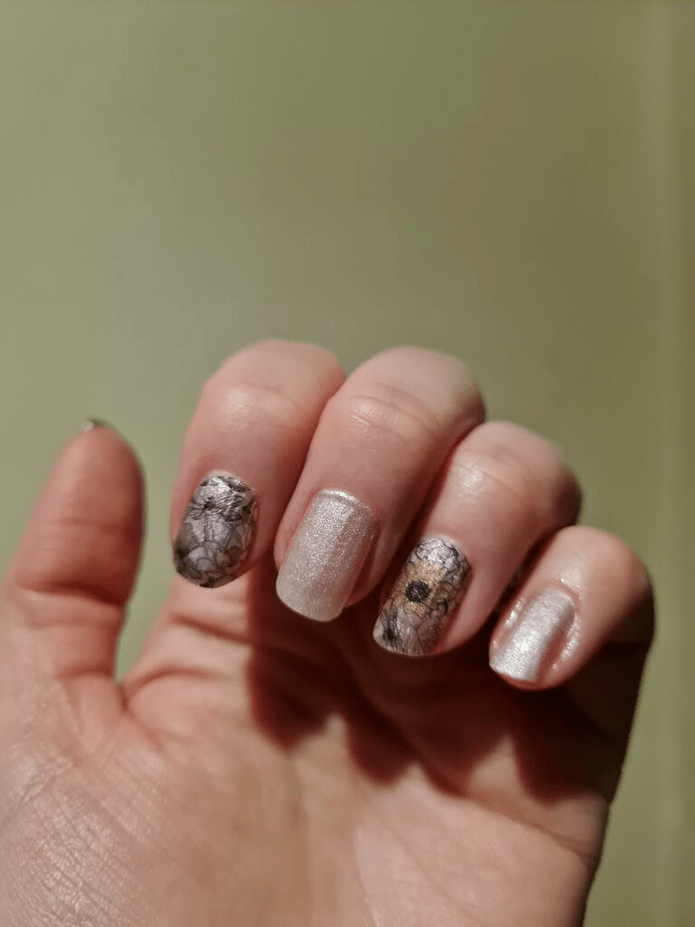 Hand showing floral nail art wraps with pink shimmer and botanical design