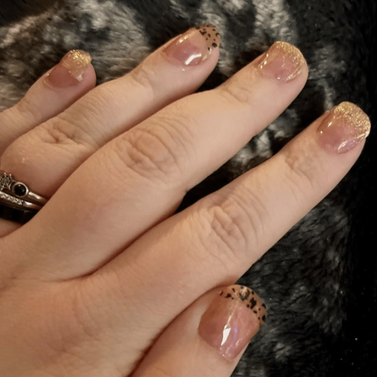 Sheer pink nail wraps with gold glitter tips and black speckled accent nail