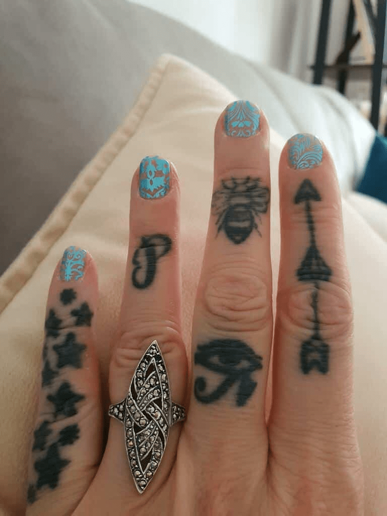 Teal ornate lace pattern non-UV nail wraps on tattooed hand with decorative ring