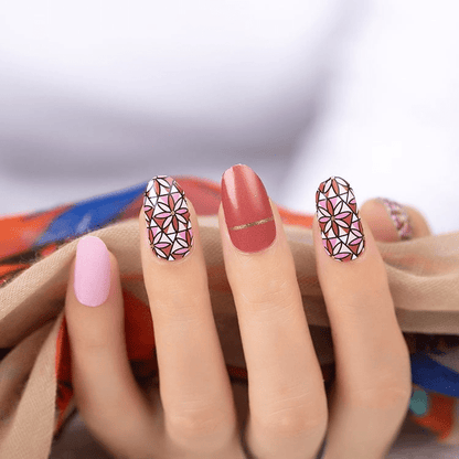 Pink and red nail art wraps with white geometric patterns on hand for at-home manicure