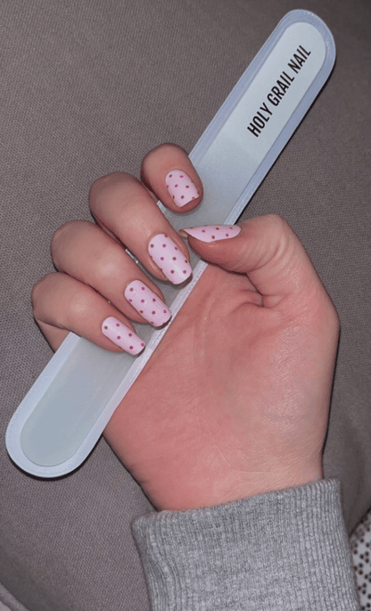 Hand applying pink polka dot nail wraps using nail file for manicure