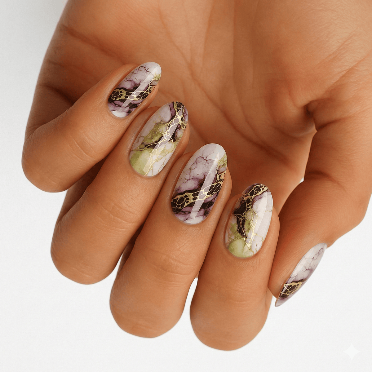 Hand wearing marble effect nail wraps in sage green and mauve with metallic accents