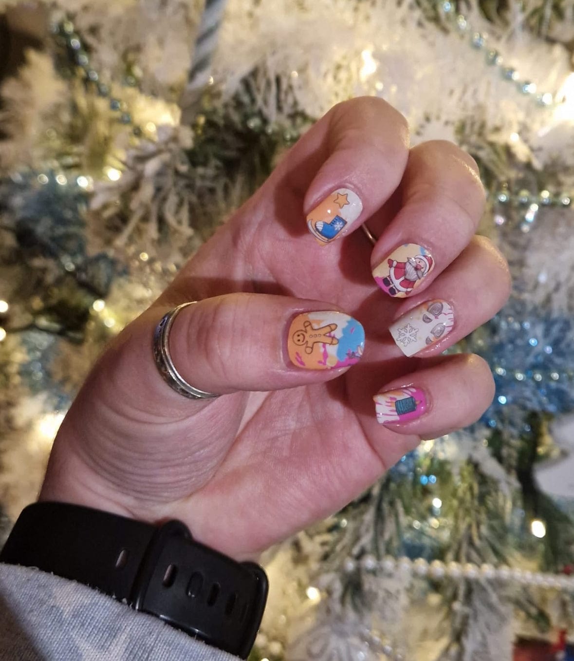 Christmas nail art featuring Santa and holiday cartoon designs on hand with festive tinsel background